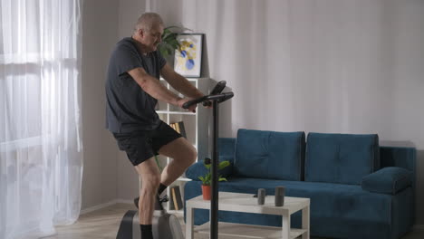 keeping-fit-and-good-physical-condition-by-workout-on-stationary-bike-middle-aged-man-is-training-alone-at-home-healthy-lifestyle-at-self-isolation